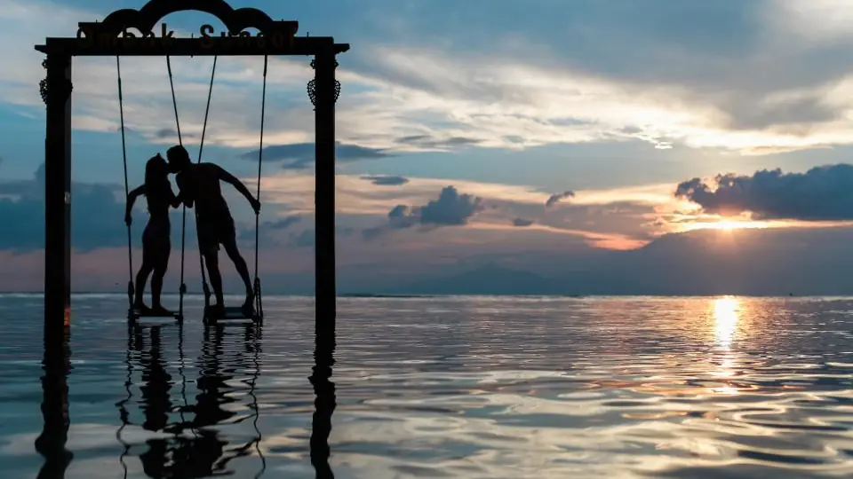 Rencontre plan cul dans le canton de Vaud: un couple qui s’embrasse sur une balançoire au-dessus de l’eau au coucher du soleil